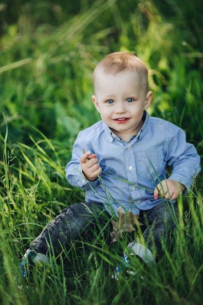 Foto retrato de niño rubio elegante sentado en el parque entre hierba