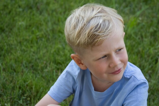 Foto retrato de un niño rubio mirando hacia el lado contra el telón de fondo de un espacio de copia de césped verde