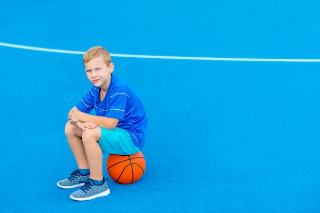 Retrato de un niño sentado en una pelota de baloncesto en la corte