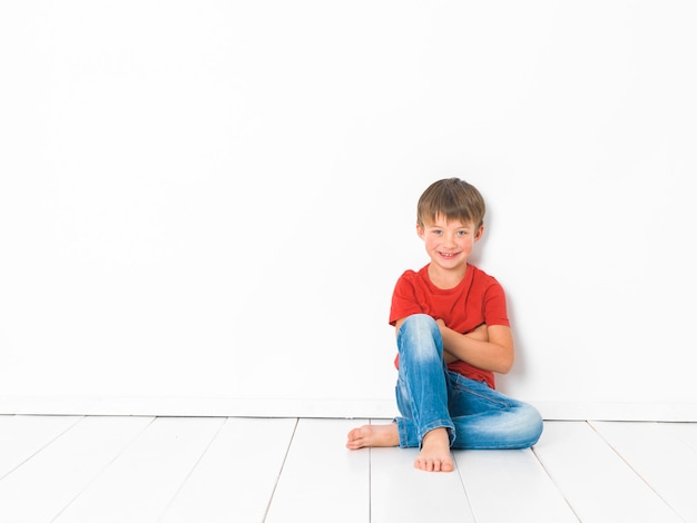 Retrato de un niño sentado en un piso de azulejos contra una pared blanca