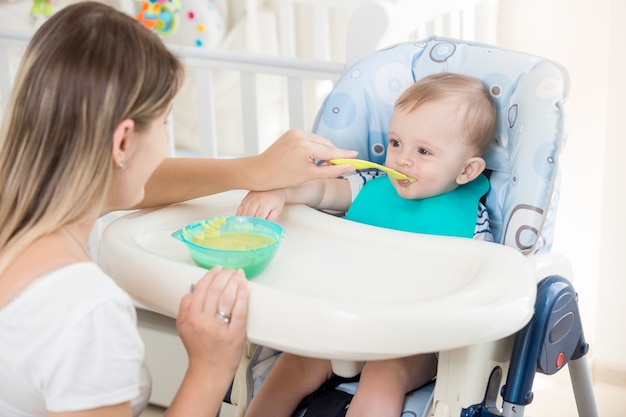 Retrato de niño sentado en una silla alta y comer gachas de avena