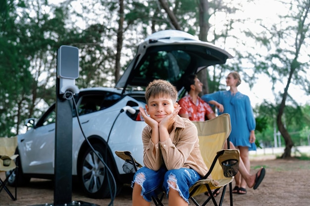 Retrato de un niño sentado en una silla de campamento con su familia en el fondo Viaje por carretera con estación de carga de energía alternativa para el concepto de automóvil ecológico Perpetual