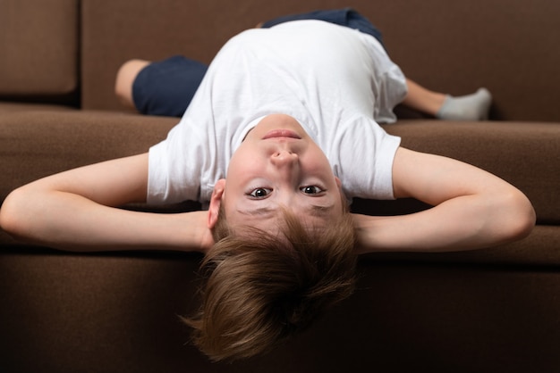 Retrato de niño en el sofá boca abajo. Niño descansando en el sofá en casa.