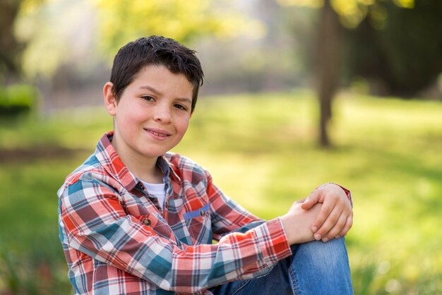 Foto retrato de un niño sonriendo mientras está sentado en el parque