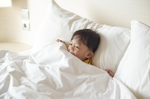 Retrato de un niño sonriente acostado y usando una manta en la cama mientras mira televisión