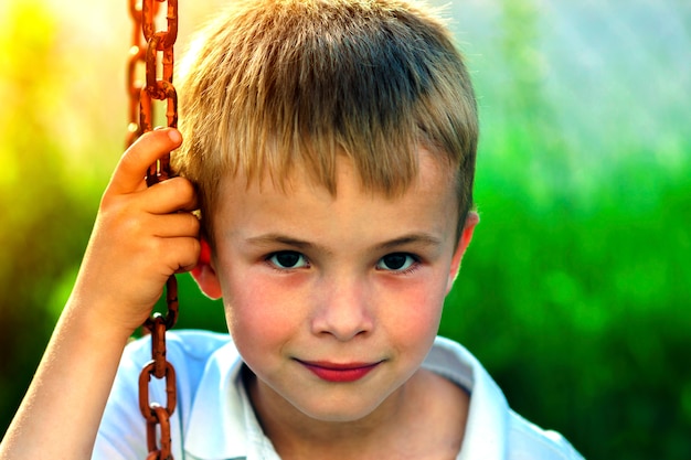 Retrato de un niño sonriente con cabello rubio paja dorado en un día soleado de verano en verde fondo borroso