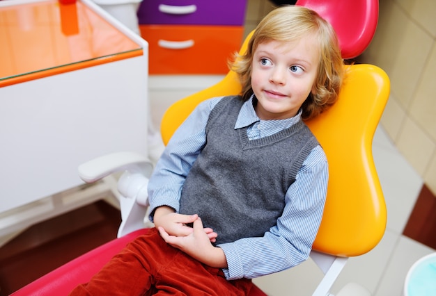 Retrato de un niño sonriente con cabello rubio rizado en el examen en una silla dental.