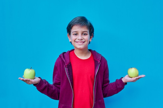 Un retrato de niño sonriente con camisa roja sosteniendo una manzana en cada mano