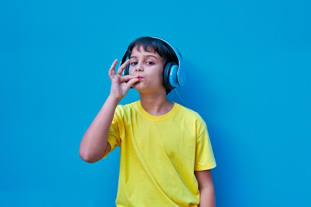 Un retrato de niño sonriente en camiseta amarilla y auriculares azules haciendo muy buen gesto