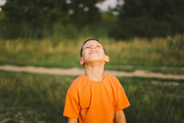 Foto retrato de un niño sonriente con una camiseta naranja y jugando al aire libre en el campo al atardecer