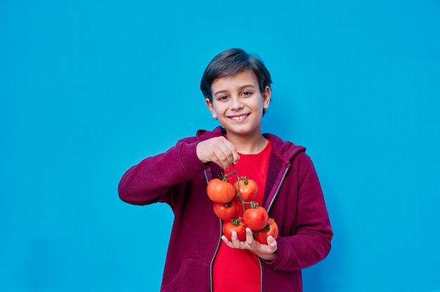 Un retrato de niño sonriente en camiseta roja enseñando tomates en la rama