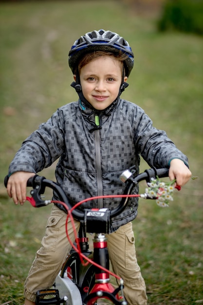 Foto retrato de niño sonriente en un casco con una bicicleta en el parque.