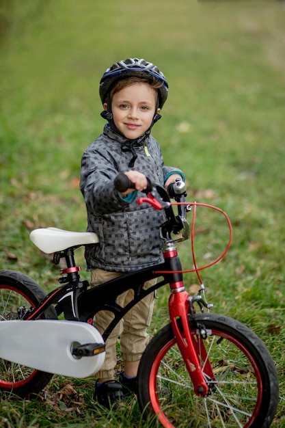 Foto retrato de niño sonriente en un casco con una bicicleta en el parque