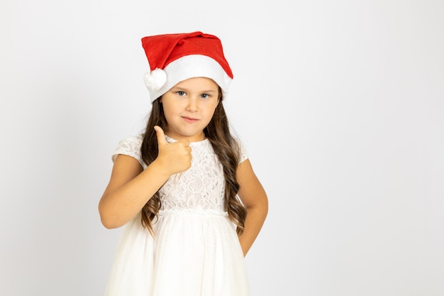 Retrato de niño sonriente entusiasta con sombrero rojo de santa claus da pulgar hacia arriba aislado sobre fondo blanco ...