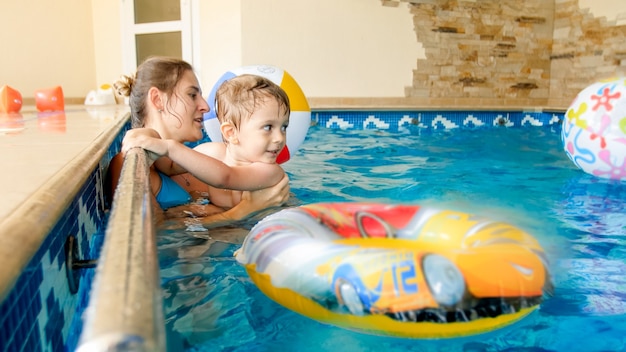 Retrato de niño sonriente feliz jugando con pelota de playa colorida inflable con la madre en la piscina interior