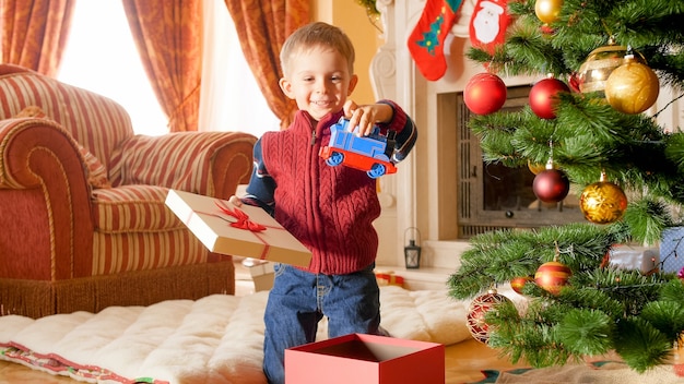 Retrato de niño sonriente feliz sacando el tren de juguete de la caja de regalo de Navidad