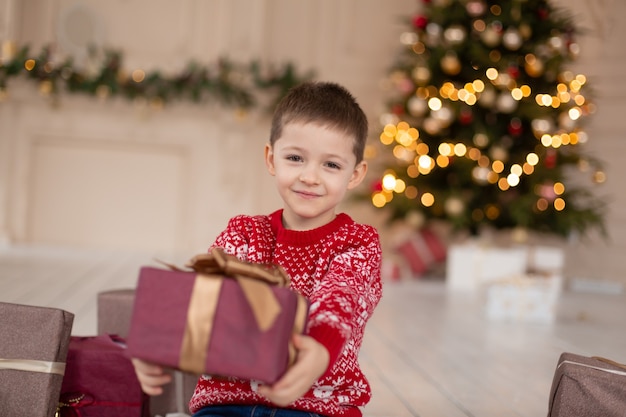 Retrato de niño sonriente feliz en suéter de punto rojo con caja actual