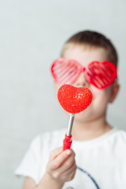 Retrato de un niño sonriente con gafas en forma de corazón en una camiseta blanca sobre un fondo blanco