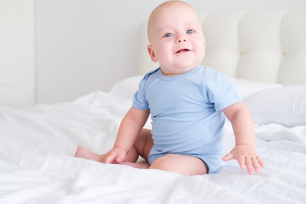 Retrato de niño sonriente con grandes ojos azules en mono sobre ropa de cama blanca Niño recién nacido sano