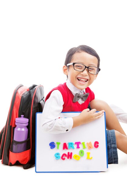 Foto retrato de un niño sonriente con una mochila sentado sobre un fondo blanco