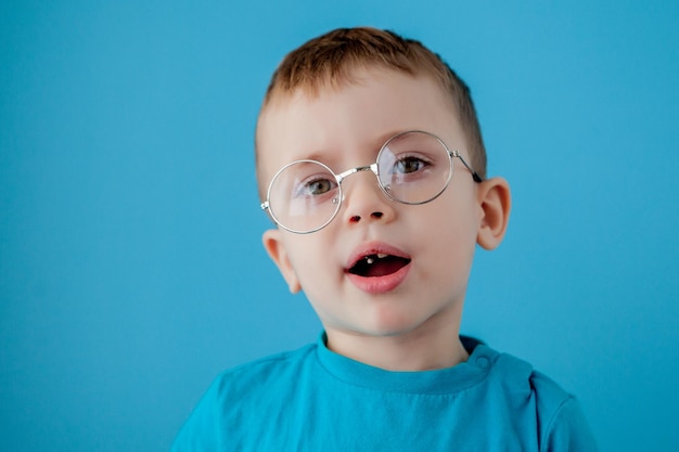 Retrato de un niño sonriente en un retrato de estudio de moda preescolar de la escuela de gafas divertidas en un espacio de copia de fondo azul