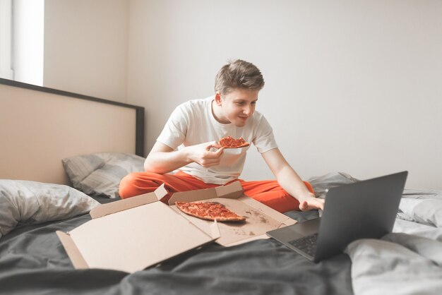 Retrato de un niño sonriente sentado en una cama con una caja de pizza