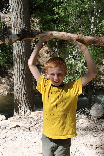 Foto retrato de un niño sonriente sosteniendo una rama en el bosque