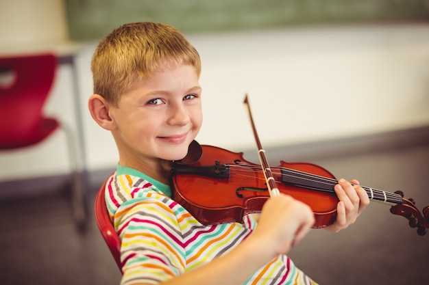 Retrato de niño sonriente tocando el violín en el aula