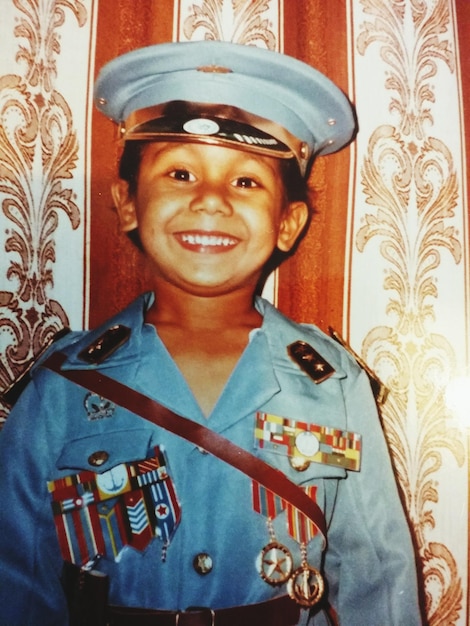 Retrato de un niño sonriente con uniforme militar contra la cortina