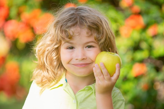 Retrato de niño sosteniendo y comiendo una manzana sobre fondo verde de la naturaleza