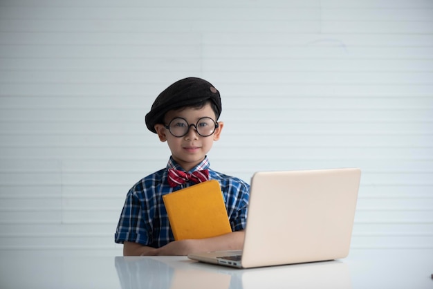 Retrato de un niño sosteniendo un libro con un portátil en el escritorio