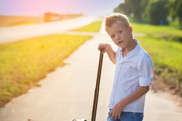 Retrato de niño tiene el asa de una maleta en el día soleado