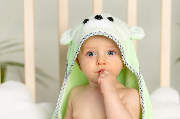 Retrato de un niño en una toalla verde después de un baño en la cama en casa con un dedo en la boca