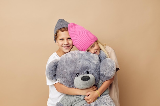 Retrato de niños lindos en sombreros con un fondo aislado de la amistad del oso de peluche