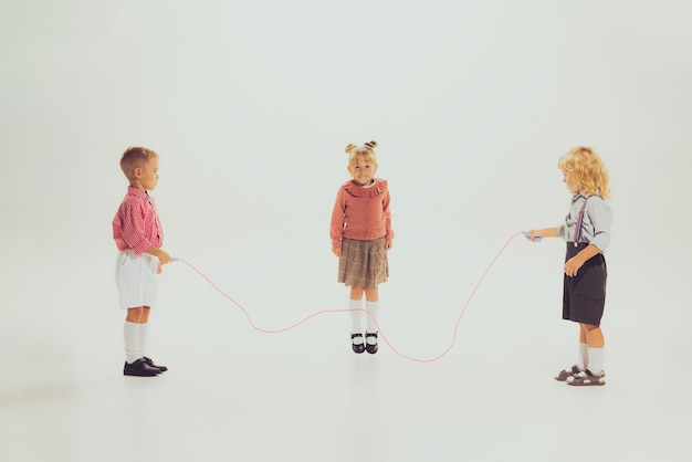 Retrato de niños y niñas jugando juntos saltando sobre una cuerda aislada sobre un estudio gris