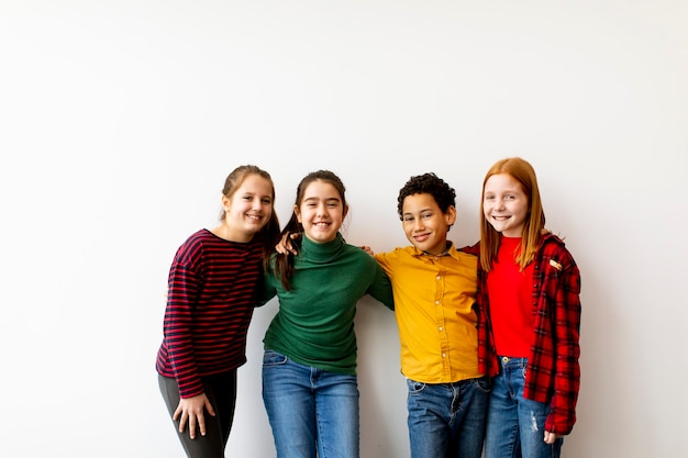 Foto retrato de niños pequeños lindos en jeans mirando a la cámara y sonriendo, de pie contra la pared blanca