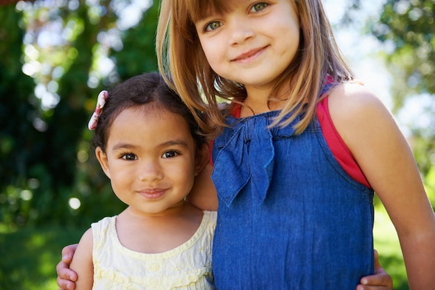 Retrato de niños y sonrisa para una cita de juego en un parque de jardín o bosque en un día soleado en Nueva Zelanda Niñas felices o hermanas adoptadas para un abrazo en la diversidad de amigos o foto de familia en primavera o verano