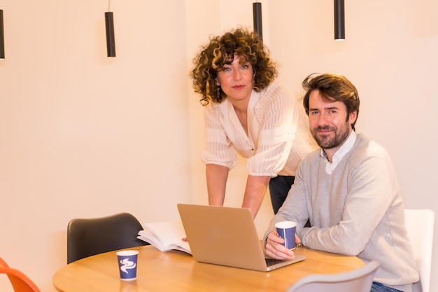 Retrato no escritório o chefe feminino e o jovem trabalhador em uma mesa no escritório com um computador e um notebook