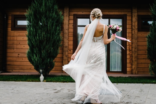 Retrato de una novia atractiva con un ramo de novia bailando y girando hacia atrás en una ceremonia de boda