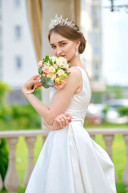 Retrato de novia bonita con corona en pelo al aire libre cerca del pabellón de ceremonia