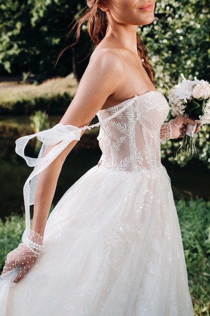 Retrato de una novia elegante en un vestido blanco con un ramo de flores en la naturaleza en un parque natural. Modelo en un vestido de novia y guantes y con un ramo. Bielorrusia.