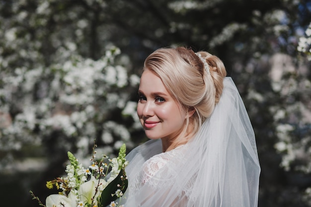 Retrato de una novia feliz con un peinado y un ramo de flores al aire libre