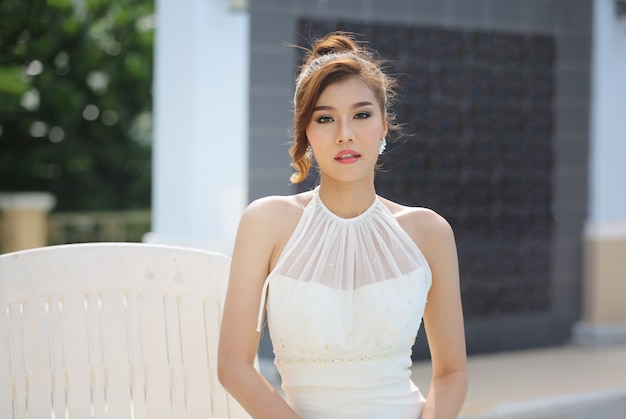 Retrato de novia hermosa en vestido de novia con falda larga y larga sentada junto a la piscina.