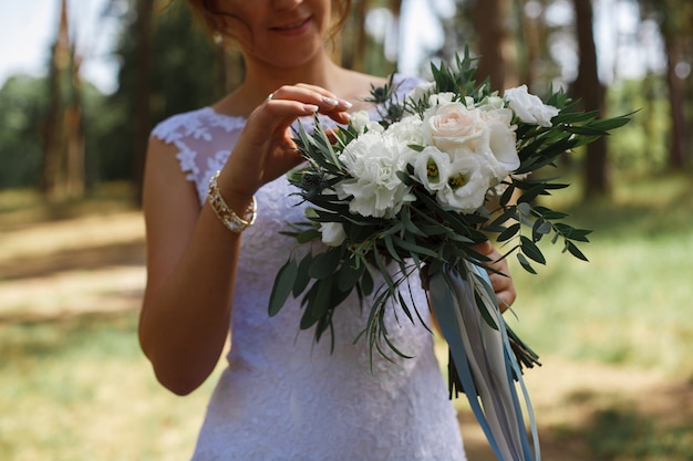 Retrato de una novia sonriente en el paseo al aire libre. Mujer joven con un ramo de flores en la primavera en un día soleado. Hermoso ramo de flores blancas y rosas. detalles de la boda