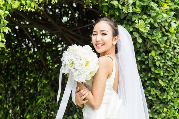 Foto retrato de la novia sonriente con un ramo de flores de pie contra las plantas