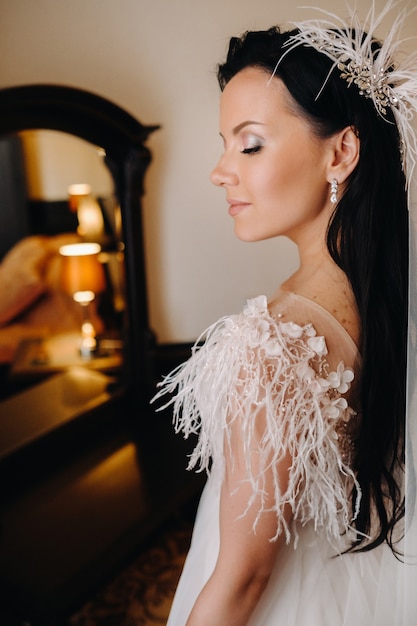 Retrato de la novia en un vestido de novia en el interior de la casa cerca del espejo