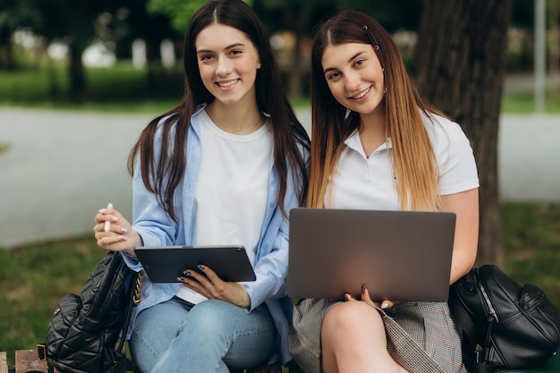 Retrato de novias estudiantes sonrientes usando laptop y tablet para estudiar en el parque