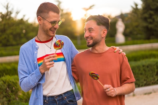 Foto retrato de novio y novia gay comiendo una piruleta en el parque al atardecer en la ciudad concepto de diversidad y lgbt