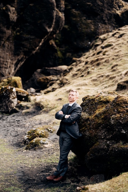 Retrato de un novio recostado sobre una piedra en un musgo junto a una hendidura rocosa con un río de montaña