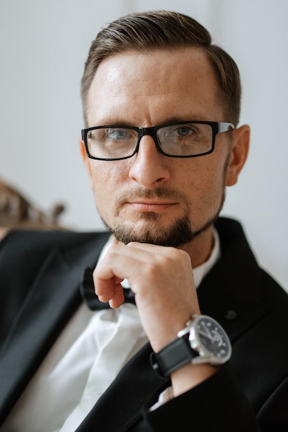 Retrato de un novio con traje negro y gafas en un estudio.